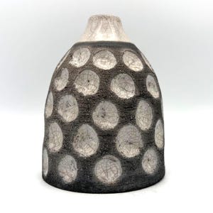 May include: A ceramic vase with a rounded shape and a narrow neck. The exterior features a dark, textured charcoal-coloured surface contrasted by circular indentations with a light grey, crackled glaze finish that reveals fine web-like patterns.