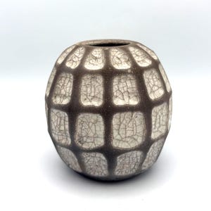 May include: A spherical ceramic vase featuring a dark brown grid pattern over a cream-coloured surface. The cream sections display a fine, intricate crackle glaze texture, while the dark brown grid lines have a matte, slightly textured finish.