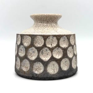 May include: A ceramic vase with a wide, short neck and a rounded body. The surface features a cream-coloured crackle glaze on the upper section and a repeating pattern of circular indentations with a dark brown, textured finish on the base.
