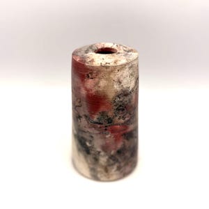 May include: A cylindrical vase featuring a mottled surface with blended tones of white, charcoal grey, and deep red. The exterior has a textured, weathered appearance with a circular opening at the top, showcasing a distinct, multi-coloured finish.