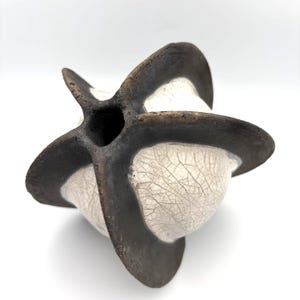 May include: A sculptural ceramic vessel featuring a spherical body with a white crackle glaze finish. The object is segmented by four prominent, dark brown, matte-textured fins that extend outward from a central opening at the top of the piece.