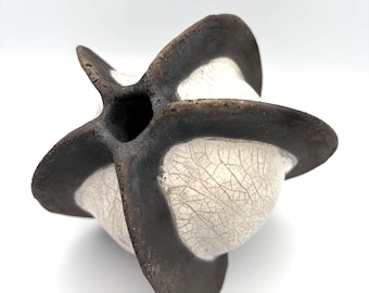 May include: A sculptural ceramic vessel featuring a spherical body with a white crackle glaze finish. The object is segmented by four prominent, dark brown, matte-textured fins that extend outward from a central opening at the top of the piece.