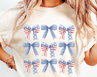 May include: A white t-shirt with a pattern of blue and red bows. The bows are decorated with a red, white, and blue American flag design.
