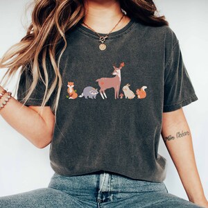 May include: A dark gray t-shirt with a graphic print of a deer, fox, raccoon, rabbit, and squirrel. The shirt has a crew neck and short sleeves.