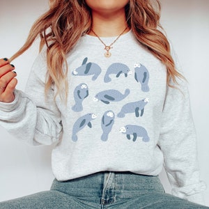 May include: A gray sweatshirt with a pattern of blue manatees. The manatees are in various poses, some swimming, some resting, and some playing.