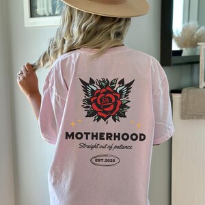 May include: Pink t-shirt with a rose and wings graphic and the text "MOTHERHOOD Straight out of patience EST. 2025"