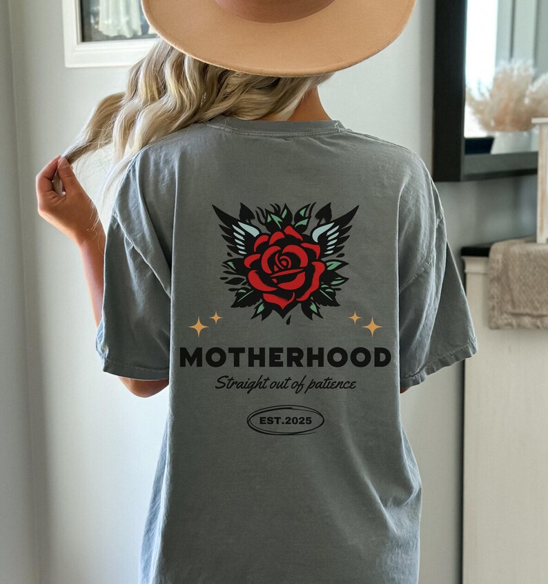 May include: A gray t-shirt with a rose and wings graphic on the back. The text "MOTHERHOOD Straight out of patience EST. 2025" is printed below the graphic.