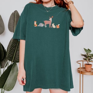 May include: A dark green t-shirt with a graphic of a deer, fox, raccoon, rabbit, and squirrel in a line. The animals are all facing the right side of the image.