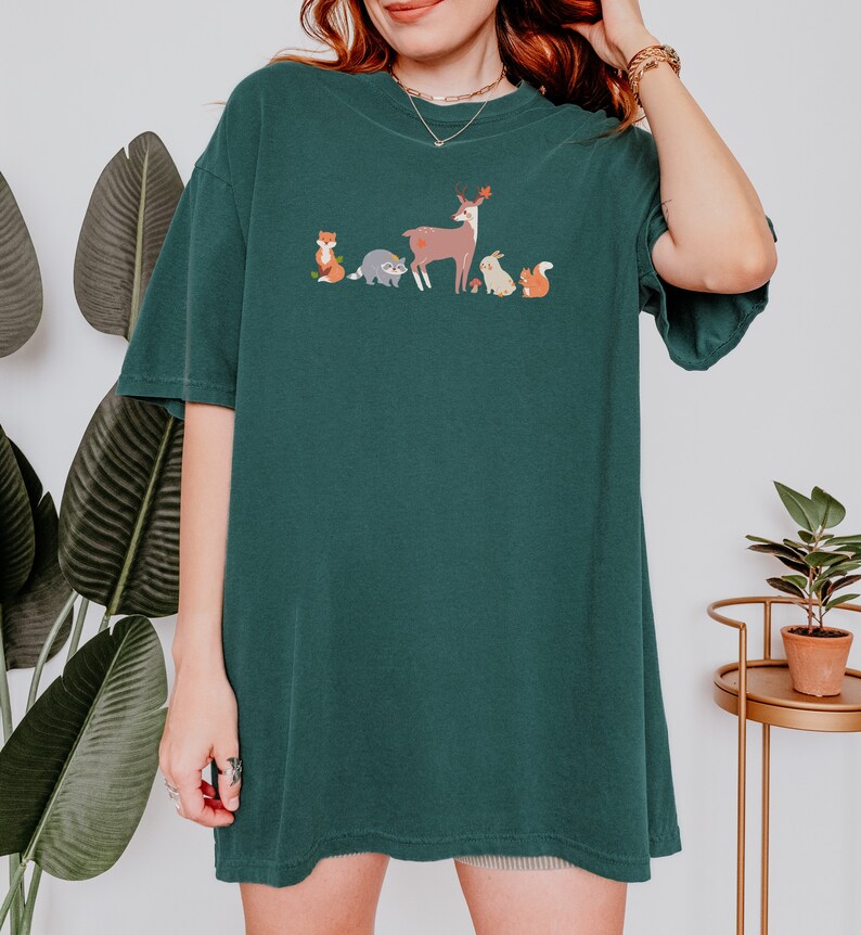 May include: A dark green t-shirt with a graphic of a deer, fox, raccoon, rabbit, and squirrel in a line. The animals are all facing the right side of the image.