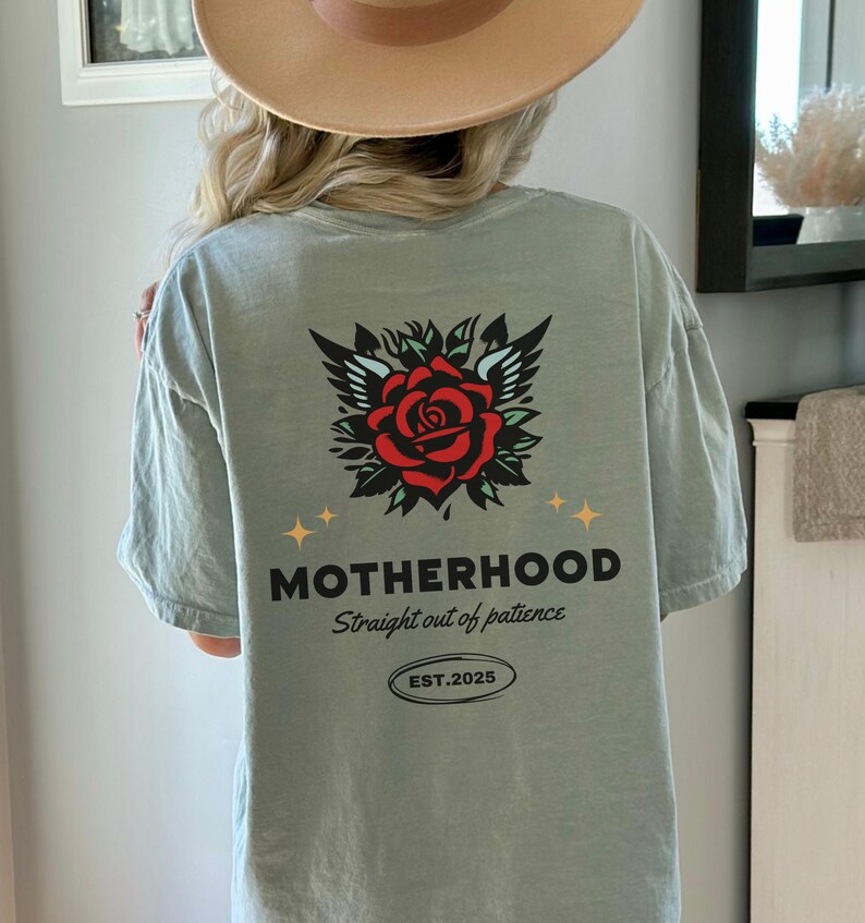 May include: A light green t-shirt with a red rose and wings graphic on the back. The text "MOTHERHOOD Straight out of patience EST. 2025" is printed below the graphic.