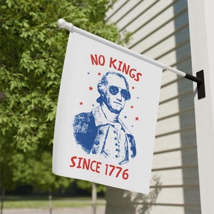 May include: White flag with a blue and red design. The flag features a portrait of George Washington wearing sunglasses, with the text "NO KINGS" above and "SINCE 1776" below. Red stars are scattered around the portrait.