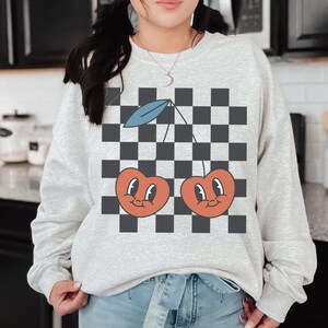 May include: A gray sweatshirt with a black and white checkered pattern and two red cherries with faces on it.