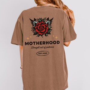 May include: Brown t-shirt with a red rose and wings graphic on the back. The text "MOTHERHOOD Straight out of patience EST. 2025" is printed below the graphic.