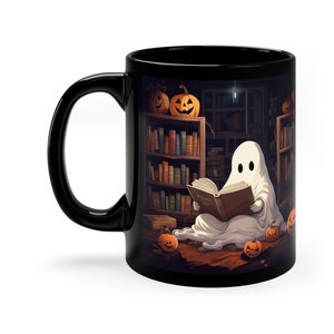 May include: A black coffee mug featuring a white ghost reading a book in a library setting. The ghost is surrounded by pumpkins and bookshelves.