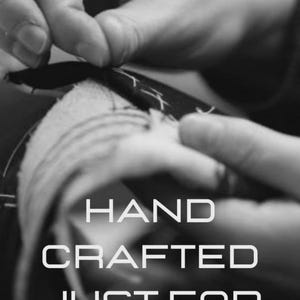 May include: Black and white image of hands sewing fabric. The text "HAND CRAFTED JUST FOR YOU" is displayed in a bold, white font. The image highlights the craftsmanship and care put into handmade items.