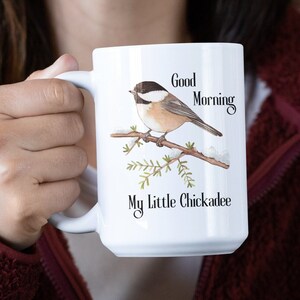 May include: White ceramic mug with a black and brown chickadee bird perched on a snowy branch. The mug has the text "Good Morning My Little Chickadee" printed on it.
