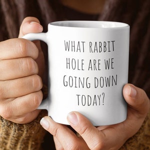 May include: White ceramic coffee mug with black text that reads "What rabbit hole are we going down today?"