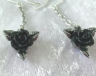 May include: A pair of silver-toned drop earrings featuring black rose pendants. Each earring has a chain that connects the hook to the rose. The rose pendants have detailed leaves with red accents.