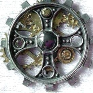 May include: A detailed, steampunk-style pendant featuring a silver-colored gear design with gold-colored inner gears and a central, dark, reflective stone. The pendant has a complex, layered construction with rivets and circular accents, suggesting a mechanical theme.
