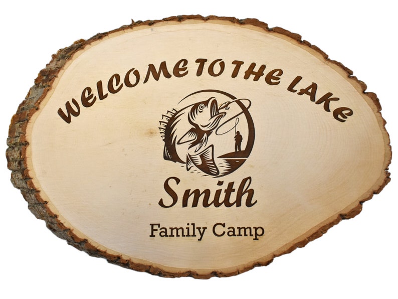 May include: Oval wooden sign with a natural bark edge. The sign reads "WELCOME TO THE LAKE" and features a fishing-themed graphic with the name "Smith" and "Family Camp" below. The wood has a light, natural finish.