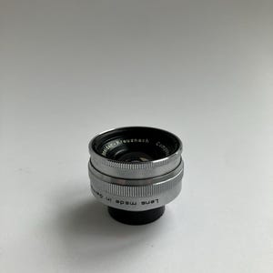 Puede incluir: Un objetivo de c&aacute;mara plateado y negro con el texto "Schneider-Kreuznach" y "Lens made in Germany" grabado en el lateral. El objetivo tiene un dise&ntilde;o estriado y un interior negro.