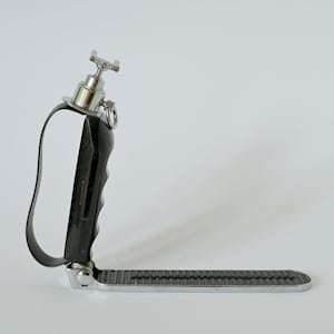 May include: A black and silver camera accessory with a handle and a textured base. The handle is black with a curved design, and the base is a silver-colored metal. The top has a silver-colored knob.