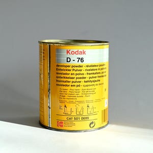 May include: A yellow metal can of Kodak D-76 developer powder. The can has text in multiple languages, including English, French, German, Spanish, Italian, and Portuguese. The text describes the product as a developer powder for photographic film. The can also has a product code: CAT 501 0699.