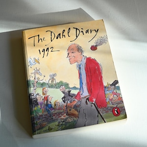 Op de afbeelding: De omslag van het boek "The Dahl Diary 1992" toont een cartoonillustratie van Roald Dahl met een groep kinderen en dieren. De omslag is geel met zwarte tekst.