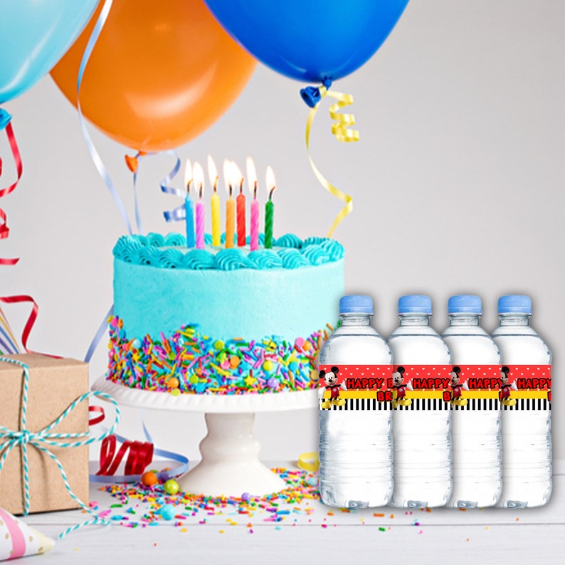 K&ouml;nnte beinhalten: Vier durchsichtige Plastikwasserflaschen mit roten und schwarzen Etiketten, auf denen "Happy Birthday" steht und ein Cartoon-Bild von Mickey Mouse abgebildet ist. Die Flaschen stehen auf einem wei&szlig;en Holztisch mit einer blau-wei&szlig;en Geburtstagstorte und bunten Streuseln.