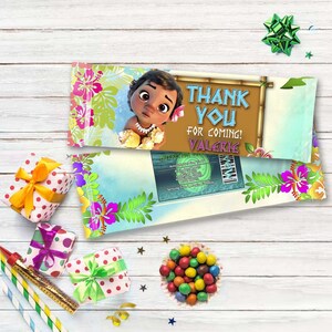 May include: A blue and green thank you favor bag with a cartoon image of a baby Moana. The bag has the text "Thank You for Coming! Valerie" printed on it.