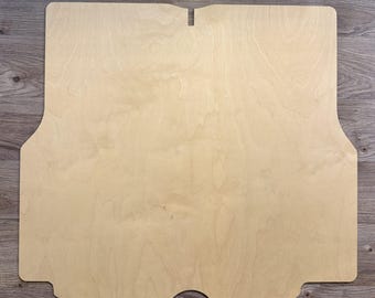 May include: A flat, light-colored wooden panel with a smooth surface and natural grain patterns. The board features a symmetrical, custom-cut shape with rounded corners, straight edges, and a small rectangular notch centered at the top edge.