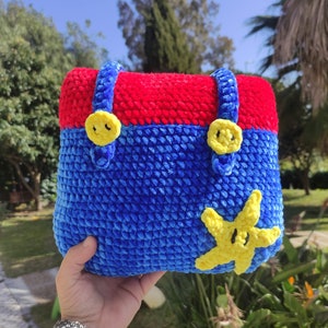 Pode incluir: Uma bolsa de crochê azul e vermelha com botões amarelos e uma estrela do mar amarela de crochê.