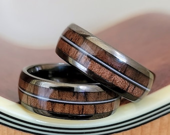 May include: Two black and brown wood rings with silver wire inlay. The rings are stacked on top of each other.