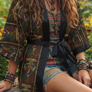 May include: A long-sleeved kimono-style robe featuring a dark, multi-colored stained glass pattern with black trim and a waist tie, worn over a patterned top and denim shorts, accessorized with layered beaded bracelets and a multi-strand necklace.
