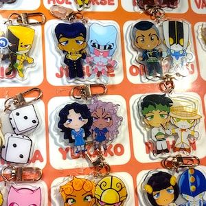 Puede incluir: Una colección de llaveros de acrílico transparente con varios pares de personajes estilo anime y cierres de mosquetón de metal dorado. Cada llavero muestra dos figuras distintas con atuendos coloridos, peinados únicos y rostros expresivos.