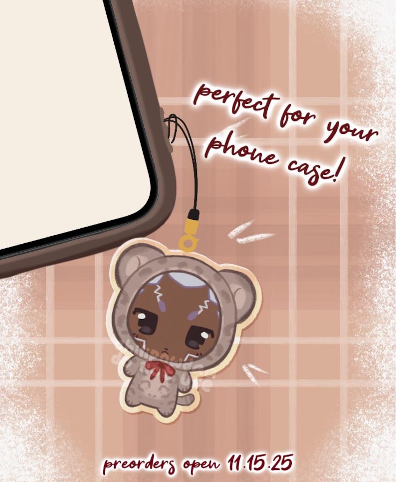 May include: A phone charm featuring a cartoon bear character in a hooded outfit with a red bow. The charm is attached to a phone case. Text reads "perfect for your phone case!" and "preorders open 11.15.25".