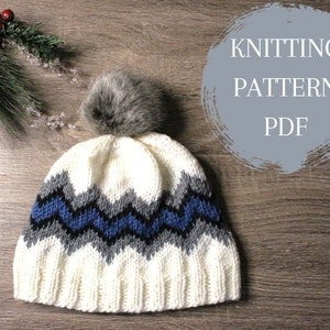 Puede incluir: Un gorro blanco de punto con un patrón de chevron azul, negro y gris y un pompón de piel sintética marrón. El gorro está sobre una superficie de madera con el texto "Knitting Pattern PDF" en un círculo.