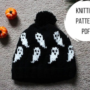 May include: Black knitted hat with a white pom pom and white ghost designs. The hat has the text "Knitting Pattern PDF" on a white circle.