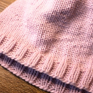 K&ouml;nnte beinhalten: Eine rosa gestrickte M&uuml;tze mit geripptem Rand.