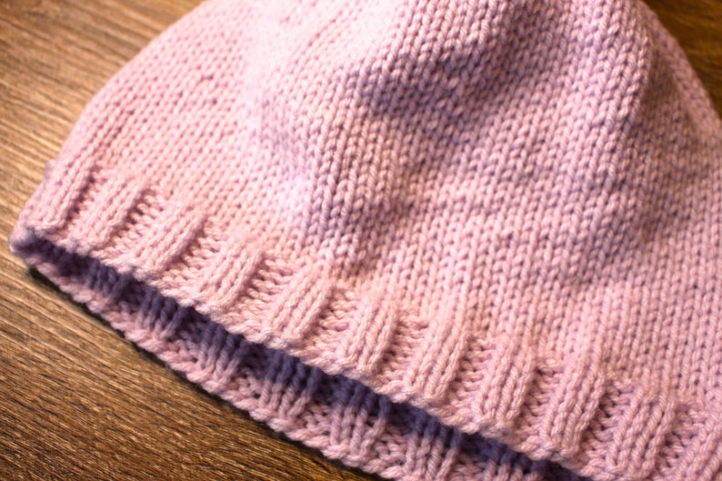 K&ouml;nnte beinhalten: Eine rosa gestrickte M&uuml;tze mit geripptem Rand.