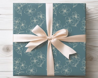 May include: A square gift box wrapped in dark teal paper featuring a repeating pattern of thin, light-colored line drawings of flowers. The box is tied with a smooth, pale cream-colored satin ribbon arranged in a centered bow on the top surface.