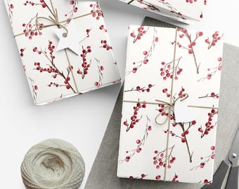 May include: Two rectangular gift boxes wrapped in white paper featuring a red berry and brown twig pattern. Each box is tied with brown twine and includes a white gift tag. A ball of white yarn, scissors, and extra white tags are present.