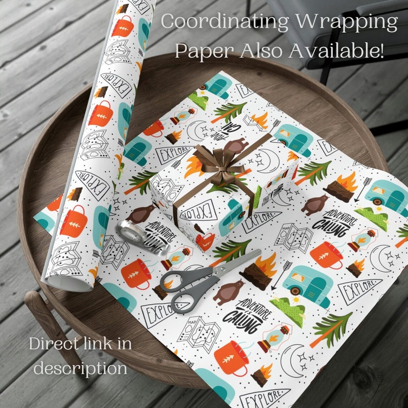 May include: White wrapping paper with a camping theme, featuring illustrations of campfires, bears, and travel trailers. A roll of paper and a wrapped gift box are visible, along with scissors and tape. The text "Explore" and "Adventure is Calling" are printed on the paper.