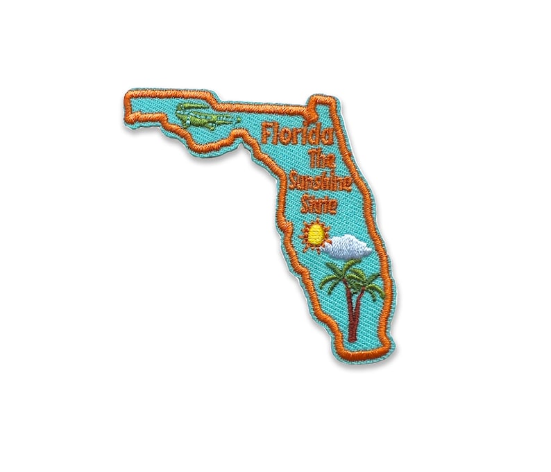 May include: An embroidered patch shaped like the state of Florida. The patch is blue with an orange outline. It says "Florida The Sunshine State" and has a small airplane, a sun, a cloud, and a palm tree.