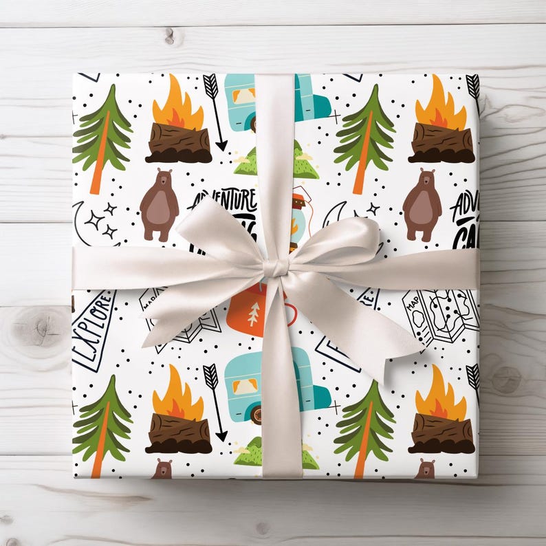 May include: White gift wrap with a camping theme, featuring illustrations of campfires, bears, trees, and a camper. The design includes the words "Adventure" and "Explore". A white satin ribbon and bow are tied around the gift.
