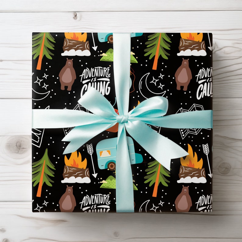 May include: A wrapped gift with black wrapping paper featuring a camping-themed pattern with bears, trees, and a camper. The text "Adventure is Calling" is visible. A light blue ribbon is tied around the gift.