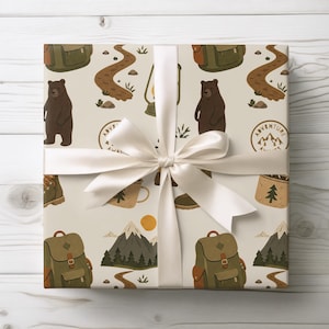 May include: Gift-wrapped package with a cream-colored paper featuring a repeating pattern of outdoor adventure elements. The design includes brown bears, backpacks, hiking boots, mountain scenes, and winding trails. A white satin ribbon and bow complete the presentation.