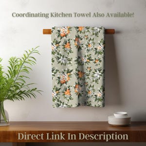 May include: A kitchen towel with a floral pattern of orange blossoms and white flowers on a light green background. The towel is hanging on a wooden rod. The text "Coordinating Kitchen Towel Also Available!" and "Direct Link In Description" are visible.