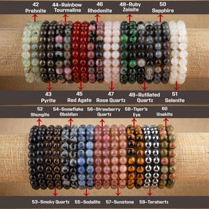 May include: A collection of 10 gemstone bracelets, each with a different type of stone. The bracelets are arranged in two rows, with the top row showing bracelets made of prehnite, tourmaline, rhodonite, zoisite, and sapphire. The bottom row shows bracelets made of pyrite, red agate, rose quartz, rutilated quartz, selenite, shungite, obsidian, strawberry quartz, tiger's eye, unakite, smoky quartz, sodalite, sunstone, and terahertz.