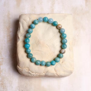 Puede incluir: Un brazalete de piedras preciosas azul claro con cuentas redondas. El brazalete est&aacute; sobre una superficie blanca.